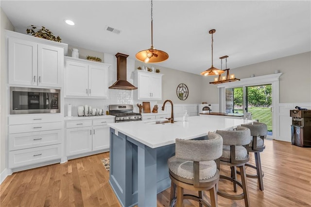 kitchen with wall chimney exhaust hood, a sink, appliances with stainless steel finishes, white cabinets, and a kitchen bar