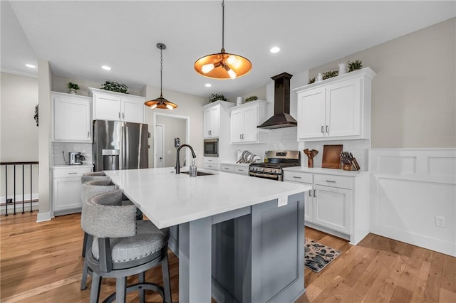 kitchen with wall chimney exhaust hood, stainless steel appliances, an island with sink, a sink, and a breakfast bar area