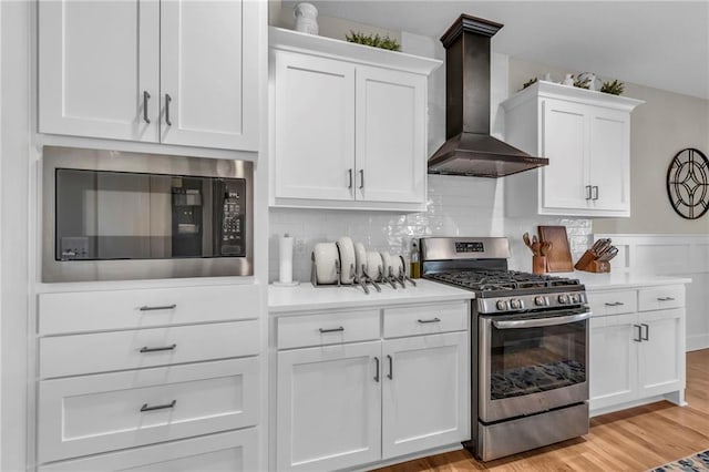 kitchen with appliances with stainless steel finishes, wall chimney range hood, white cabinets, and light countertops
