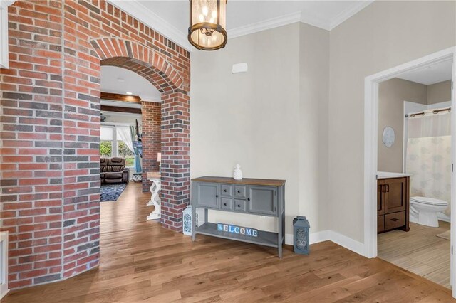 corridor with wood finished floors, ornate columns, baseboards, arched walkways, and ornamental molding