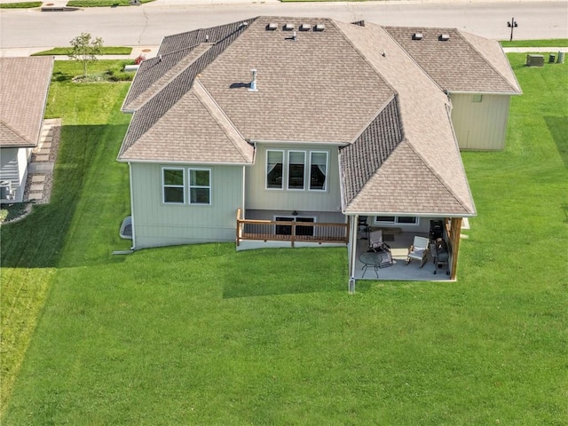 rear view of house featuring a patio, roof with shingles, and a yard