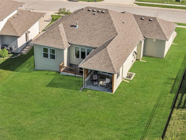 rear view of property featuring a patio area, roof with shingles, and a lawn