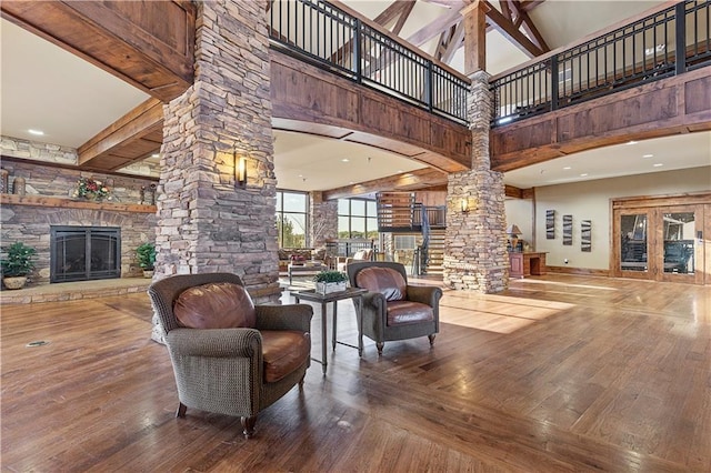 living room featuring decorative columns, a high ceiling, hardwood / wood-style floors, beamed ceiling, and a stone fireplace