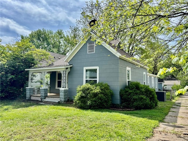 view of side of property featuring a yard, a porch, and roof with shingles