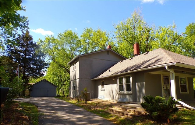 view of front facade with stucco siding, a chimney, an outdoor structure, roof with shingles, and a detached garage