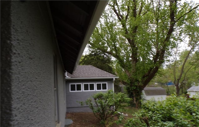 view of property exterior featuring a shingled roof, stucco siding, and a shed
