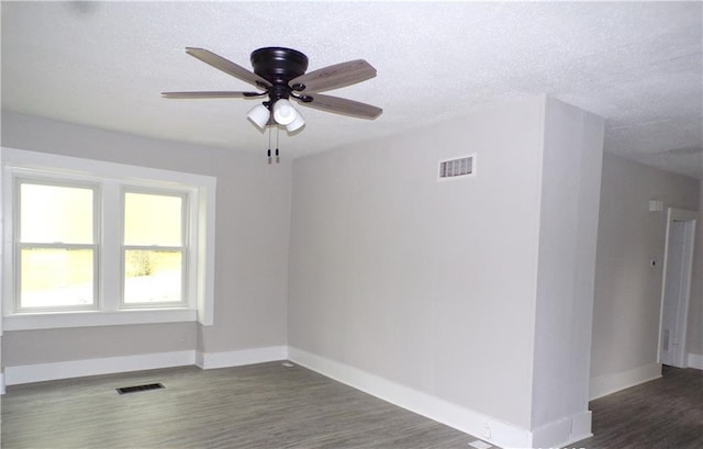 spare room featuring baseboards, a ceiling fan, visible vents, and dark wood-type flooring