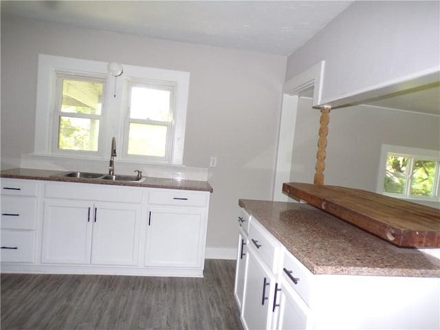 kitchen with dark stone counters, dark wood-type flooring, white cabinets, and a sink