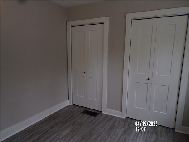 unfurnished bedroom featuring a closet, visible vents, baseboards, and dark wood-style floors