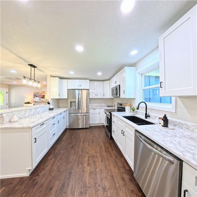 kitchen with stainless steel appliances, a sink, a peninsula, dark wood finished floors, and white cabinets