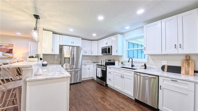kitchen featuring stainless steel appliances, a sink, a peninsula, white cabinets, and recessed lighting