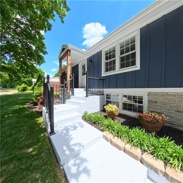 doorway to property with board and batten siding, a yard, and stone siding