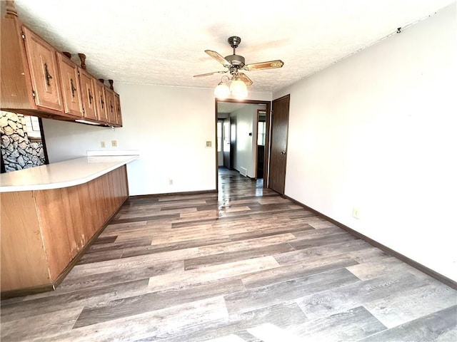 kitchen featuring brown cabinets, wood finished floors, a textured ceiling, ceiling fan, and light countertops