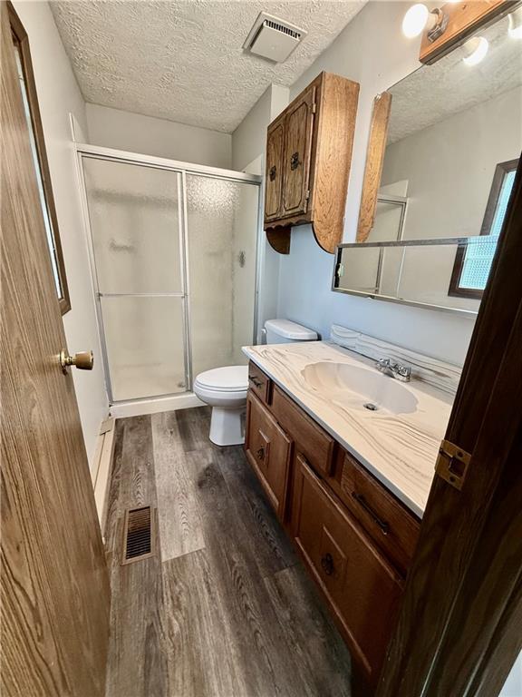 full bath with toilet, wood finished floors, a stall shower, a textured ceiling, and vanity