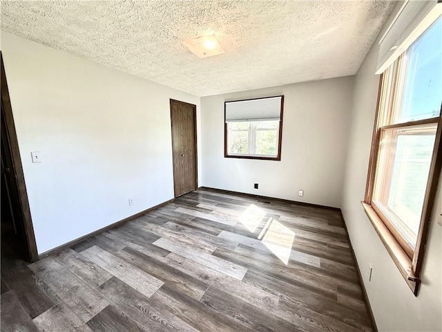 unfurnished room with a textured ceiling, wood finished floors, and baseboards