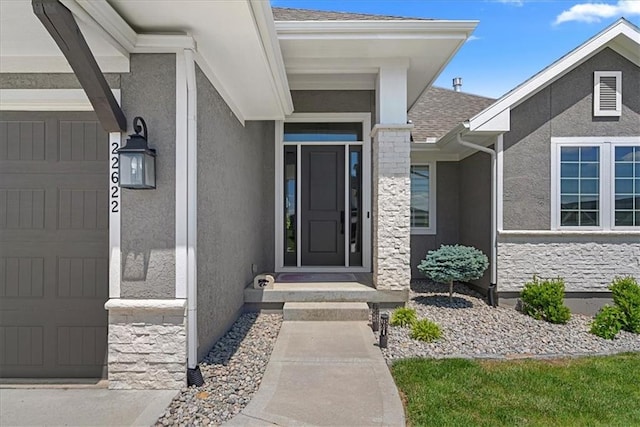 22622 W 87th Ter, Lenexa, KS 66227 - view of exterior entry with stucco siding, roof with shingles, an attached garage, and stone siding