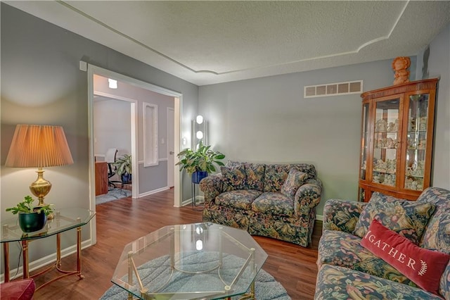 living room featuring a textured ceiling, visible vents, wood finished floors, and baseboards