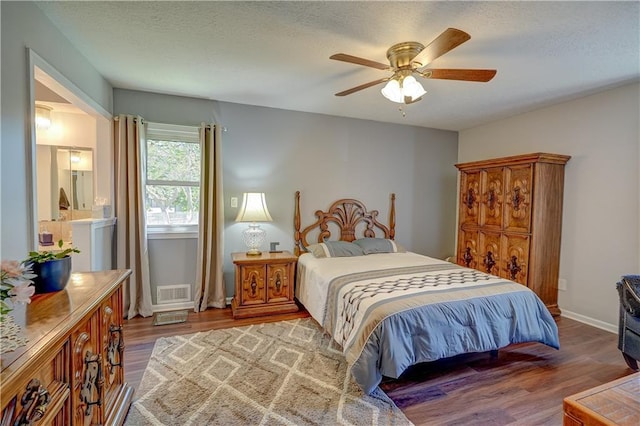 bedroom featuring a textured ceiling, a ceiling fan, visible vents, and wood finished floors