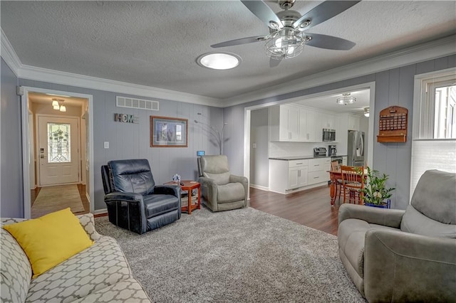 living room featuring ceiling fan, ornamental molding, a textured ceiling, and visible vents