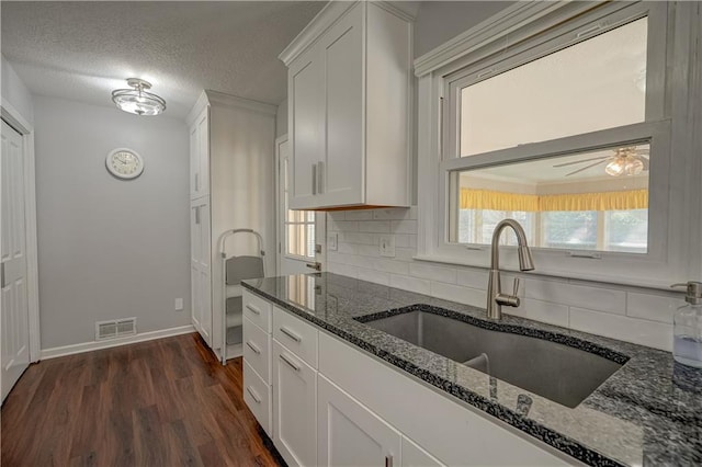 kitchen with a sink, tasteful backsplash, dark stone counters, visible vents, and white cabinetry