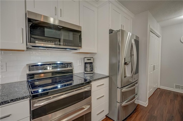 kitchen featuring dark stone counters, stainless steel appliances, visible vents, and dark wood-type flooring