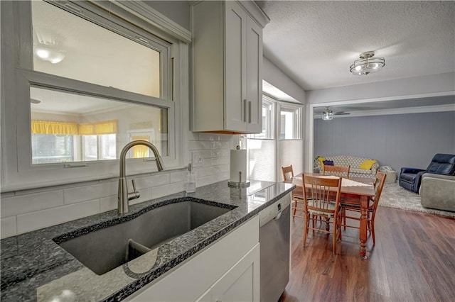 kitchen featuring dark stone countertops, a sink, dark wood-style flooring, dishwasher, and decorative backsplash