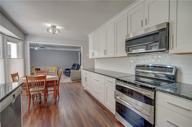 kitchen with stainless steel appliances, dark stone counters, dark wood-type flooring, decorative backsplash, and white cabinets