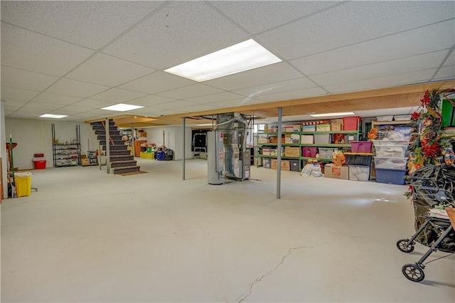 finished below grade area with a paneled ceiling, water heater, heating unit, and stairway