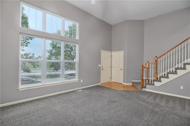 entryway with carpet, a towering ceiling, baseboards, and stairs