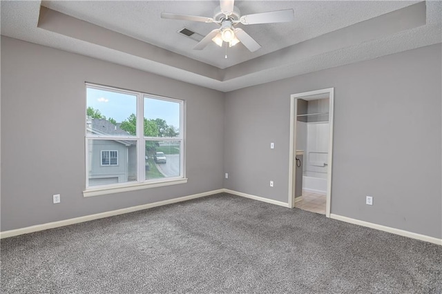 unfurnished bedroom featuring carpet floors, baseboards, a tray ceiling, a textured ceiling, and a ceiling fan