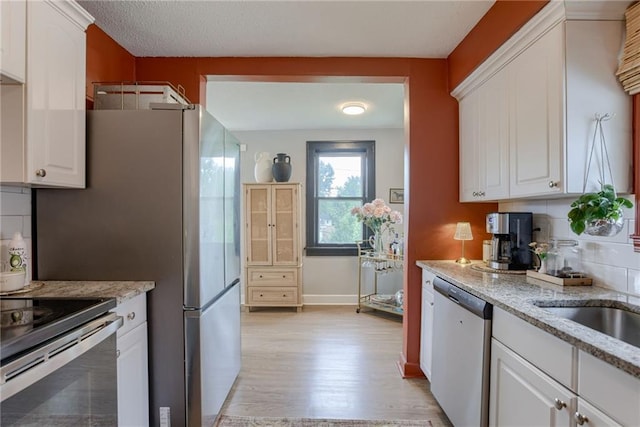 kitchen featuring appliances with stainless steel finishes, light wood-type flooring, tasteful backsplash, white cabinets, and light stone countertops
