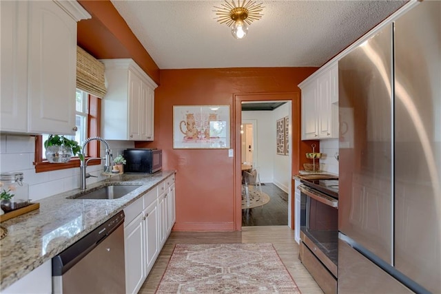 kitchen with stainless steel appliances, a sink, white cabinets, light stone countertops, and light wood finished floors