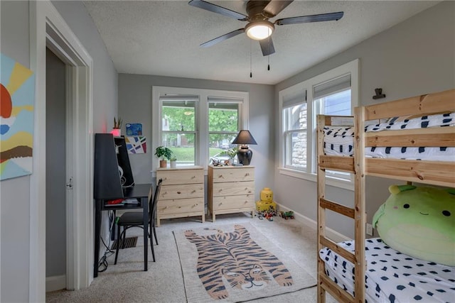 carpeted bedroom featuring multiple windows, baseboards, a desk, a textured ceiling, and ceiling fan