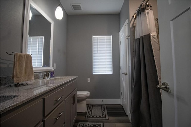 bathroom with toilet, baseboards, visible vents, a sink, and double vanity