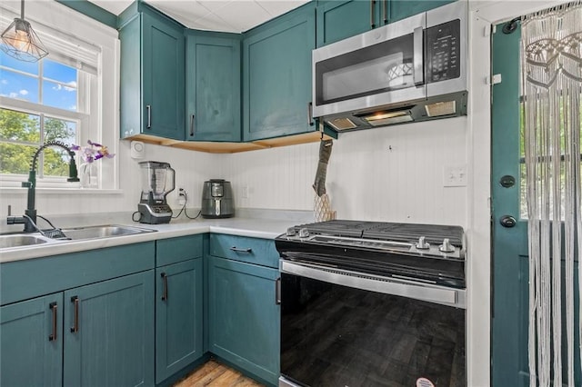 5801 E 56th St, Kansas City, MO 64129 - kitchen with appliances with stainless steel finishes, a sink, light countertops, light wood-style floors, and hanging light fixtures