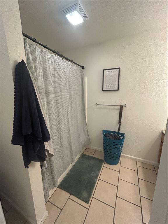 722 N Virginia St, Adrian, MO 64720 - bathroom with tile patterned flooring, a shower with shower curtain, and baseboards