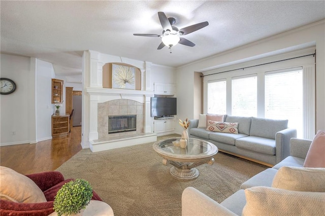 living area with a ceiling fan, a tiled fireplace, baseboards, and wood finished floors