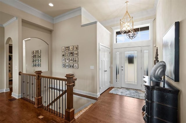 foyer entrance featuring a chandelier, wood finished floors, crown molding, baseboards, and arched walkways
