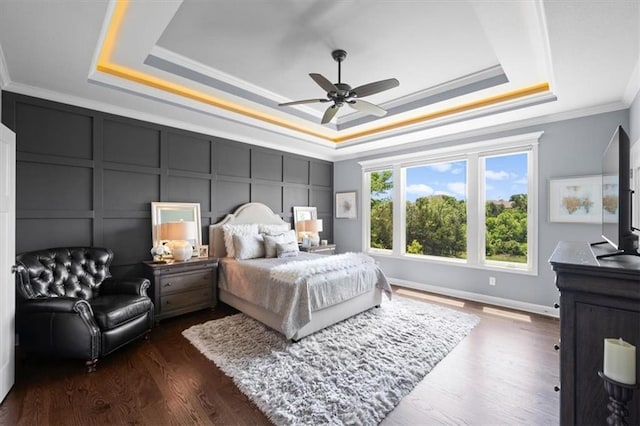 bedroom with a raised ceiling, crown molding, a decorative wall, dark wood-type flooring, and a ceiling fan