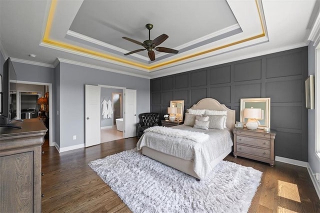 bedroom with a tray ceiling, a decorative wall, ornamental molding, baseboards, and wood finished floors