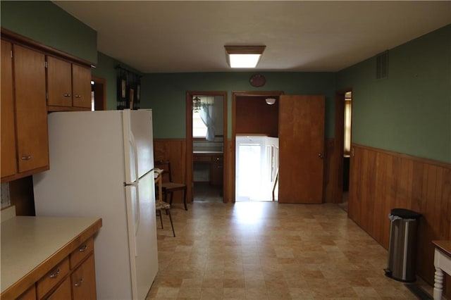 kitchen featuring freestanding refrigerator, wooden walls, and a wainscoted wall