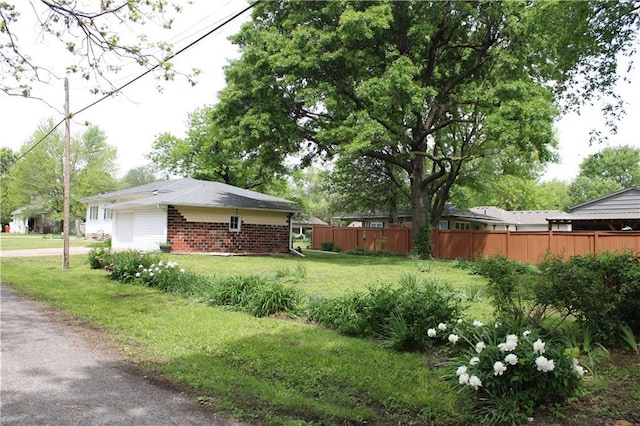 view of property exterior featuring fence, brick siding, driveway, a garage, and a lawn