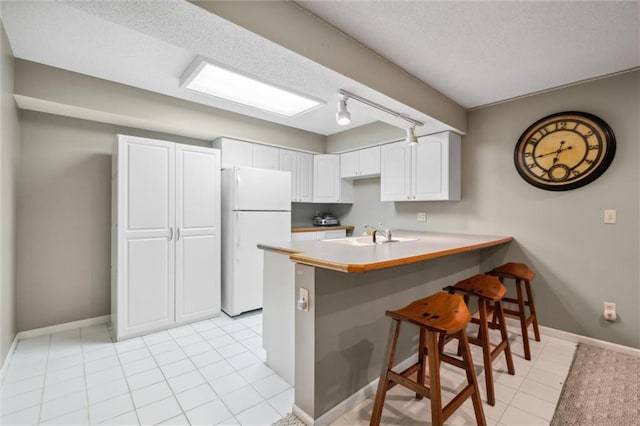 14910 Rhodes Cir, Lenexa, KS 66215 - kitchen featuring freestanding refrigerator, a peninsula, a kitchen bar, track lighting, and white cabinetry