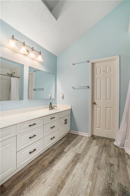 15951 S Avalon St, Olathe, KS 66062 - full bath featuring vaulted ceiling, wood finished floors, double vanity, a shower with shower curtain, and a textured ceiling