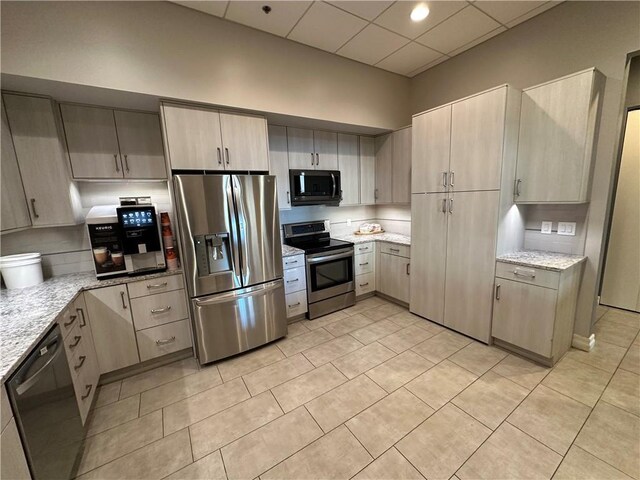 4950 Central St Unit 102, Kansas City, MO 64112 - kitchen with stainless steel appliances, light stone counters, light tile patterned floors, a paneled ceiling, and light brown cabinets