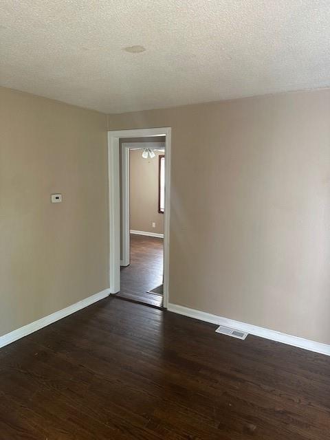 3805 Laurel Ave, Kansas City, MO 64133 - spare room with a textured ceiling, baseboards, visible vents, and dark wood finished floors