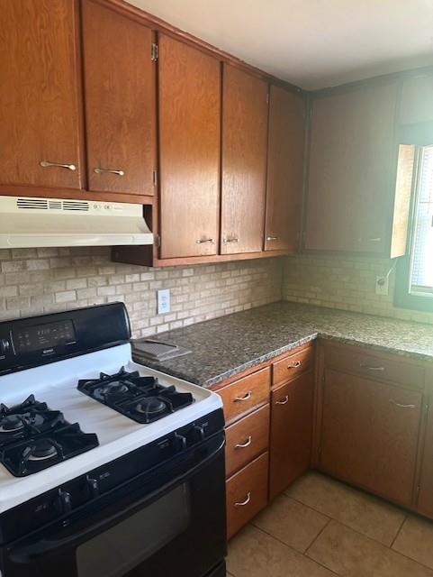 3805 Laurel Ave, Kansas City, MO 64133 - kitchen featuring black gas range oven, under cabinet range hood, light tile patterned flooring, dark stone countertops, and tasteful backsplash