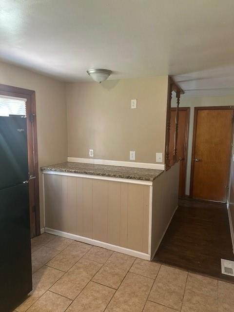 3805 Laurel Ave, Kansas City, MO 64133 - kitchen featuring freestanding refrigerator, stone counters, light tile patterned floors, and visible vents