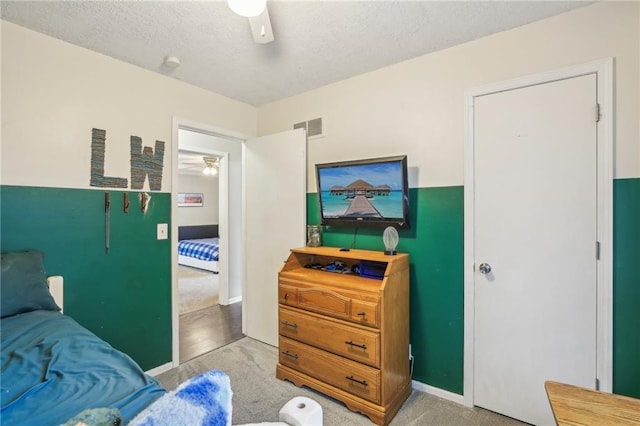 bedroom featuring light colored carpet, baseboards, ceiling fan, and a textured ceiling