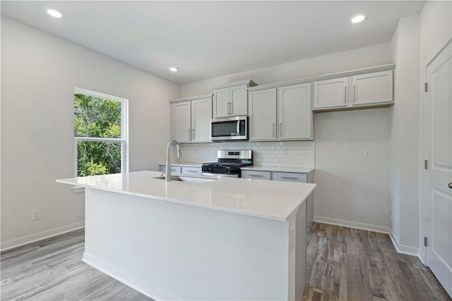 kitchen with appliances with stainless steel finishes, a sink, a center island with sink, light wood-style floors, and recessed lighting